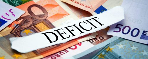Word "Deficit" printed on a piece of paper and placed above the pile of euro banknotes