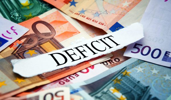 Word "Deficit" printed on a piece of paper and placed above the pile of euro banknotes